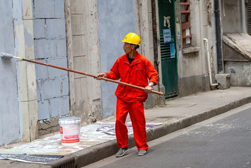 Person in orange workwear painting a building wall.