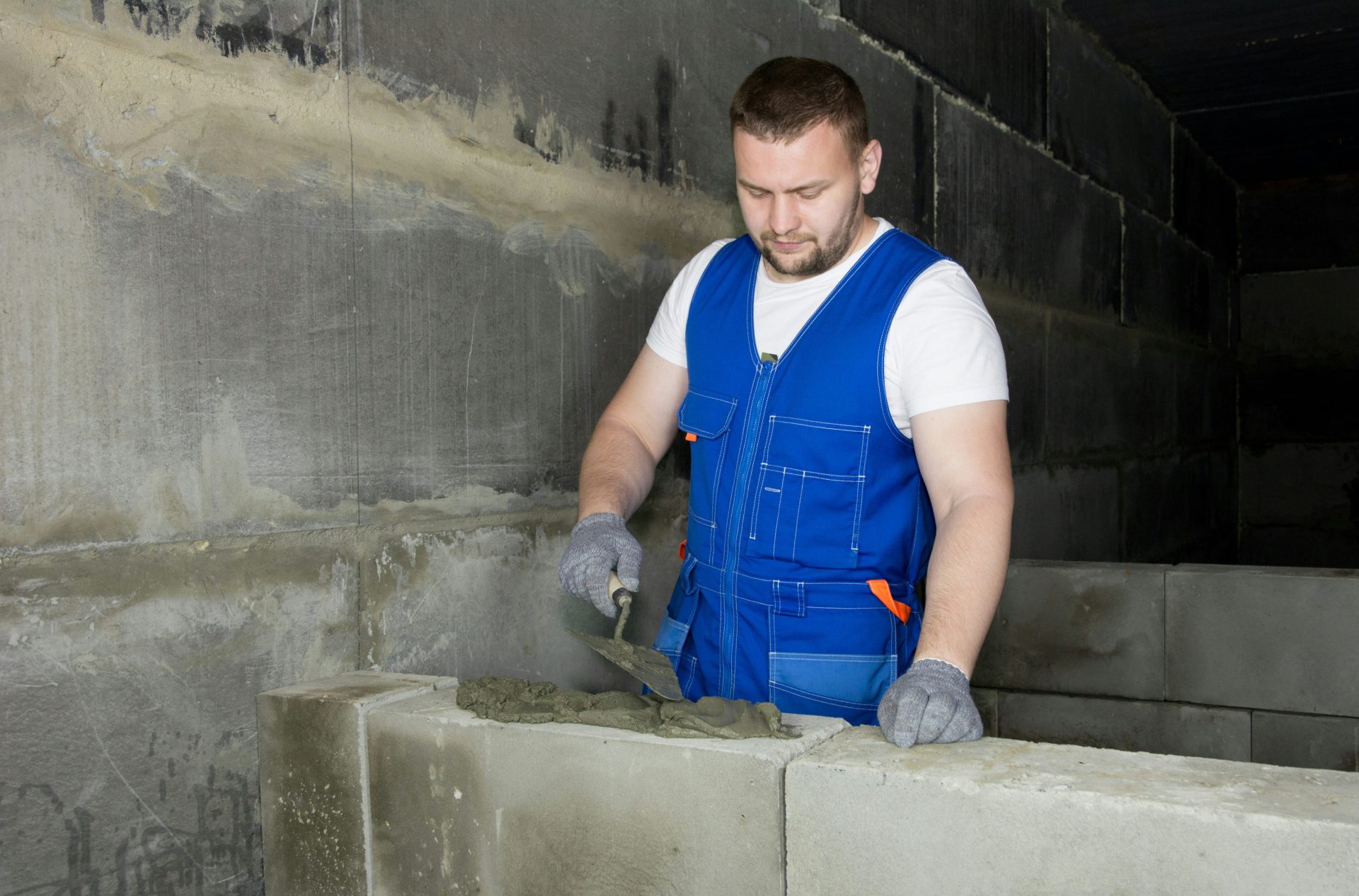 Ein Mann in einem blauen Overall, der mit Zement arbeitet.
